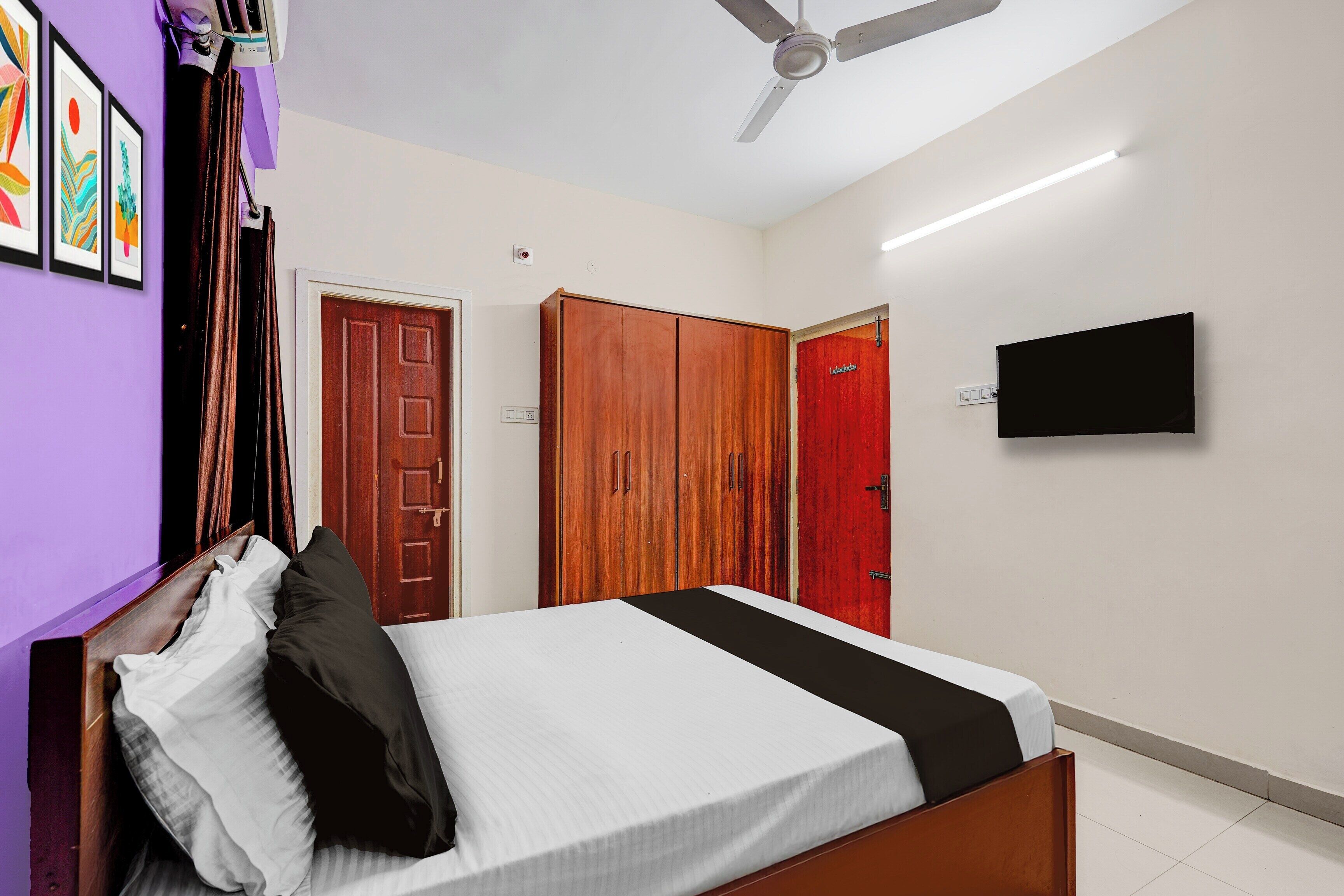 A bedroom with a bed, a ceiling fan, a TV mounted on the wall, and wooden wardrobes.