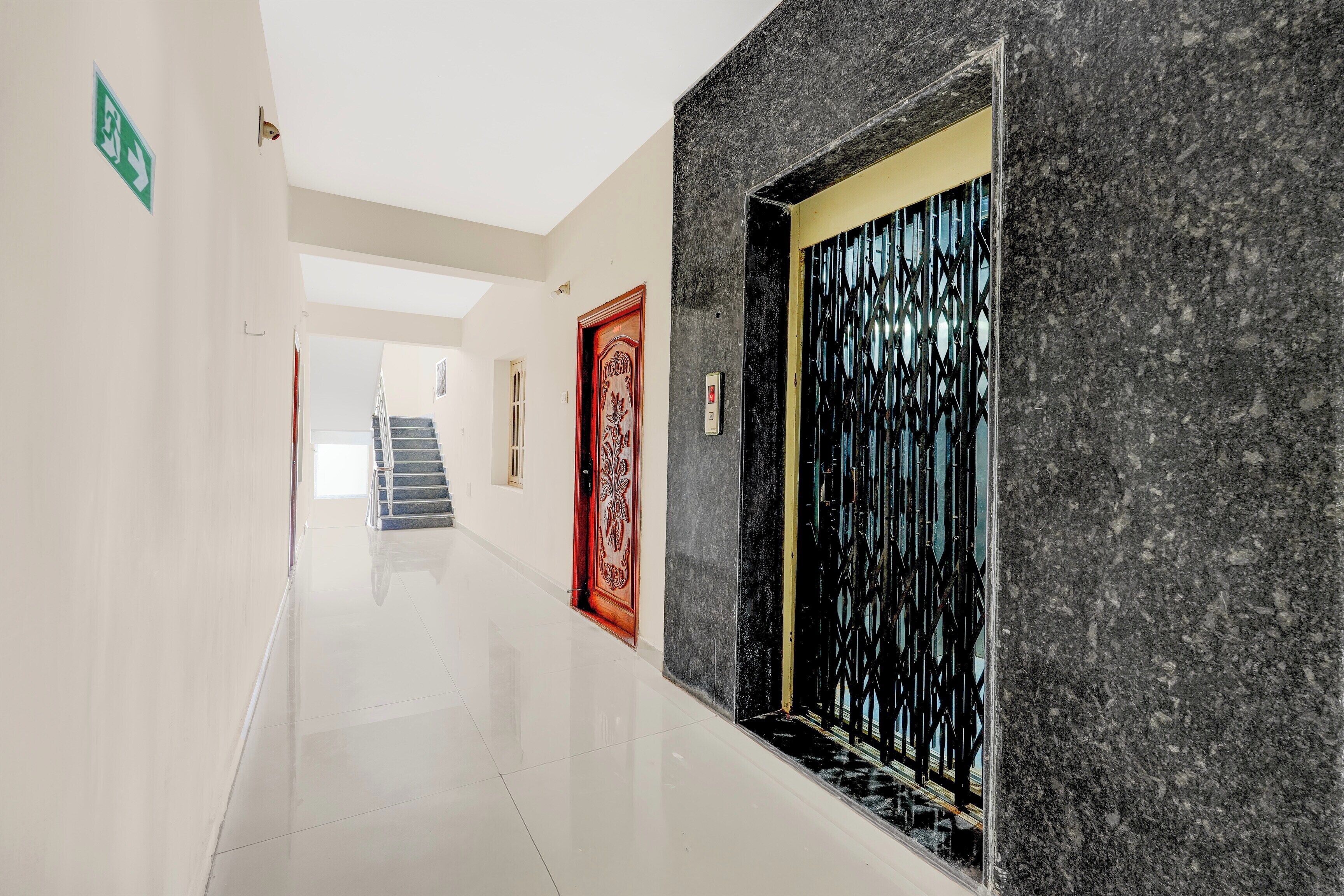 A hallway with a marble wall, a red door with intricate designs, and a staircase in the background.