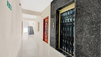A hallway with a marble wall, a red door with intricate designs, and a staircase in the background.