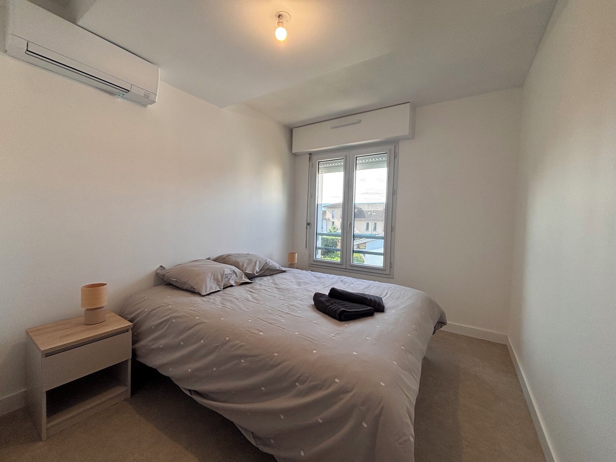 Ein Schlafzimmer mit einem Bett, einem Nachttisch, einem Fenster und einer Klimaanlage.