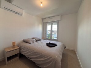 Un dormitorio con cama, mesita de noche, ventana y aire acondicionado.