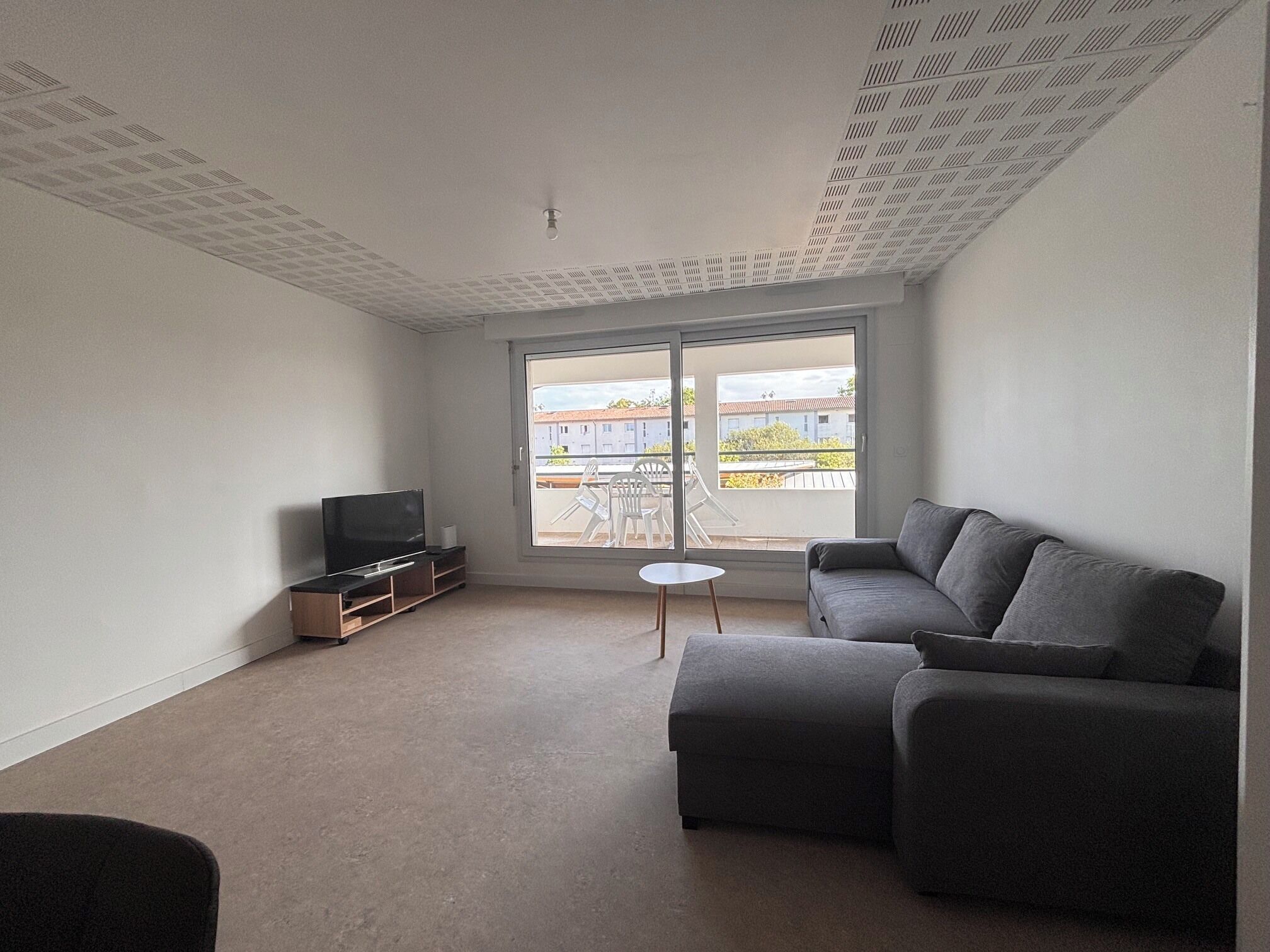 A living room with a grey sofa, a television on a wooden stand, and a small round table.