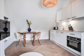 A modern kitchen with white cabinets, a built-in oven, and a dining area with a table and chairs.