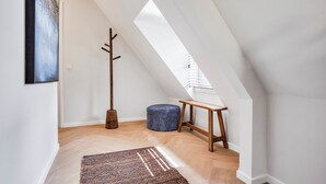 A modern loft bedroom with a sloped ceiling, a wooden coat rack, a round ottoman, and a bench. - Enjoy a stylish 50m² apartment for two in the heart of Velden. Featuring a comfortable queen bed, private kitchen, Smart TV, air conditioning, fast WiFi, and a shared balcony, it's an ideal base for both leisure and business stays. (Velden)