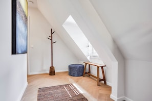 A modern loft bedroom with a sloped ceiling, a wooden coat rack, a round ottoman, and a bench. - Enjoy a stylish 50m² apartment for two in the heart of Velden. Featuring a comfortable queen bed, private kitchen, Smart TV, air conditioning, fast WiFi, and a shared balcony, it's an ideal base for both leisure and business stays. (Velden)