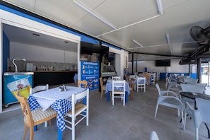 A restaurant interior with tables and chairs, a counter with a menu, and a wall with a sign. - Bed and Breakfast 'The Kavos Sandy Inn-Double Room' with Shared Pool, Wi-Fi and Air Conditioning (Kavos)