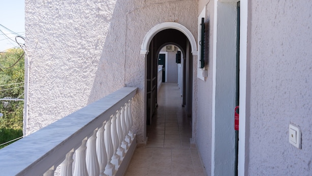 A corridor with a white balustrade, a textured wall, and a door with a red sign. - Bed and Breakfast 'The Kavos Sandy Inn-Double Room' with Shared Pool, Wi-Fi and Air Conditioning (Kavos)