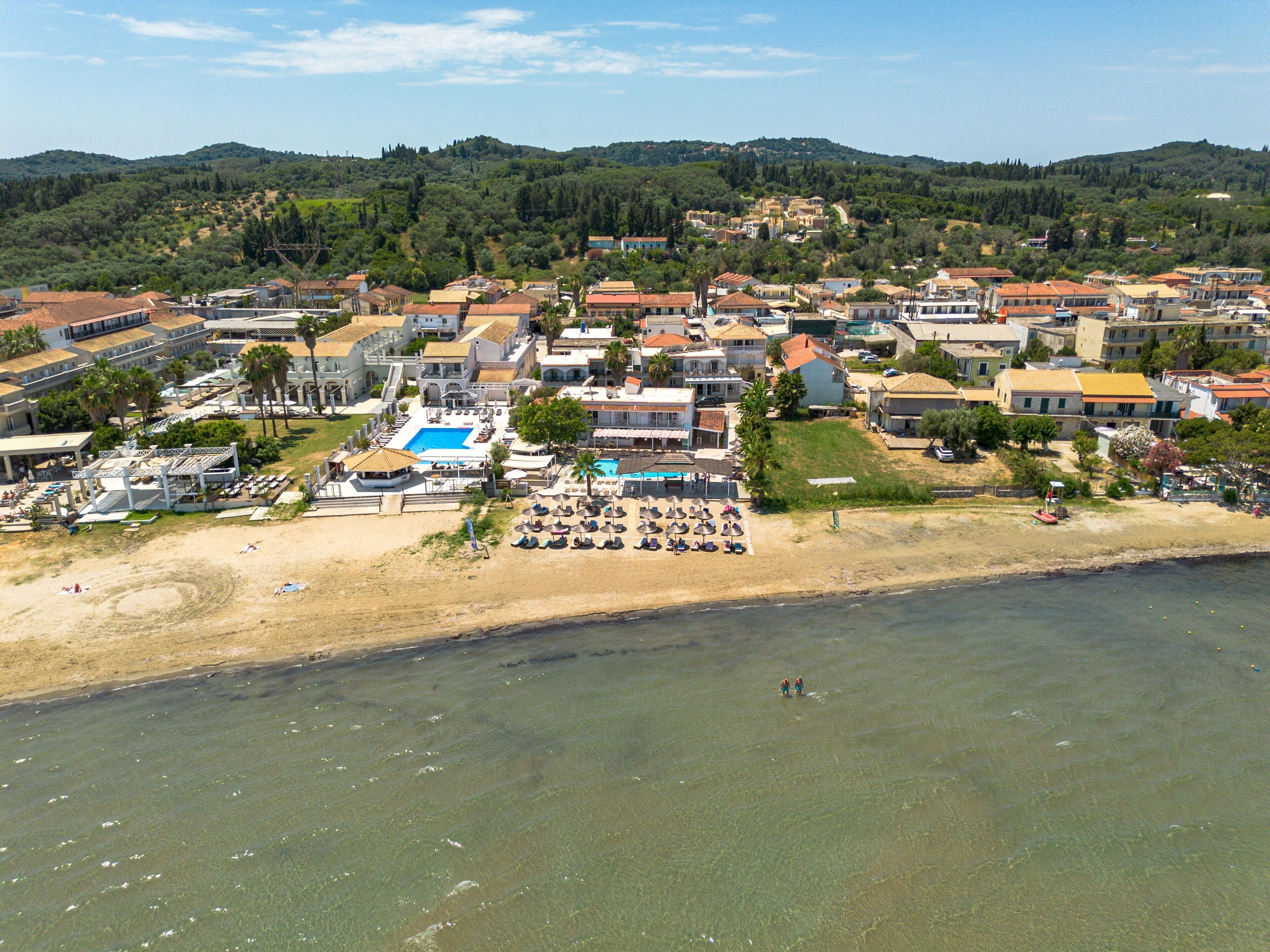 Ovenudblik over en kystresort med swimmingpool, strand og flere bygninger.