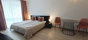 A hotel room with a bed, two chairs, a small table, and a nightstand with a lamp. - Studio in a complex with a pool (Burgas)