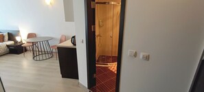 A modern hotel room with a bed, a small table, and a chair. There is a shower area visible through a glass door. - Studio in a complex with a pool (Burgas)