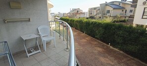 A balcony with a white chair, a small table, and a metal railing. - Studio in a complex with a pool (Burgas)