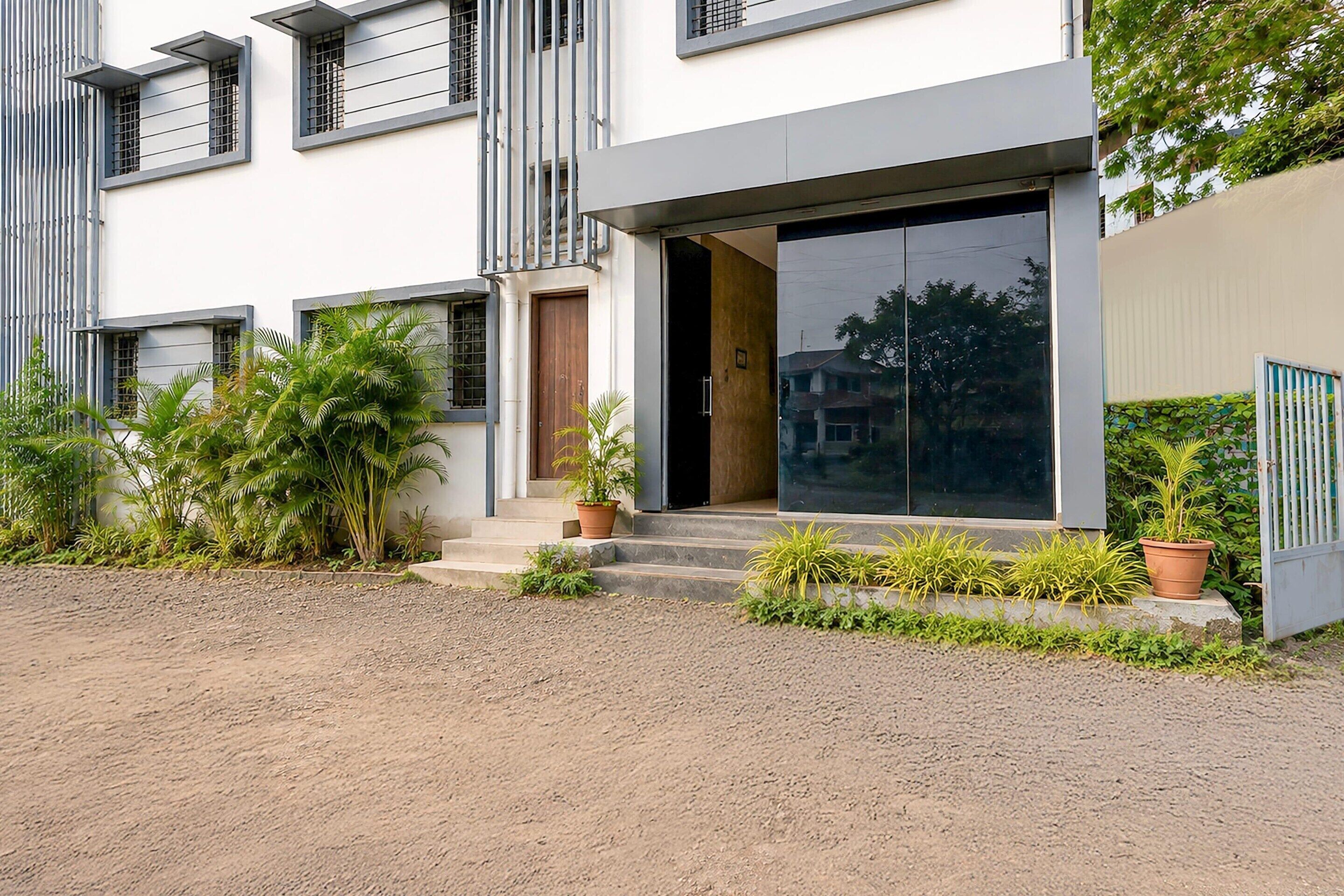 A modern two-story house with a large sliding glass door entrance, a small porch with steps, and a gravel driveway.
