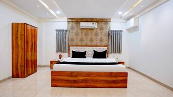 A bedroom with a large bed, wooden wardrobe, and an air conditioning unit on the wall.