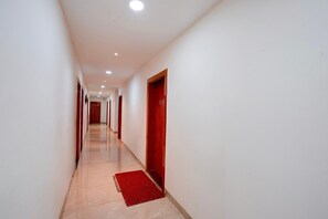 A long, narrow hallway with white walls and a red carpet leading to a wooden door. - Deluxe Room KP Pride (Pune)