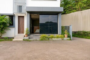 A modern house with a large glass door, a wooden door, and a concrete staircase leading to the entrance. - Deluxe Room KP Pride (Pune)