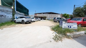 A parking lot with multiple cars, a sign for 'The Real Greek Parking,' and a building with a green tarp covering part of it. - Bed and Breakfast 'The Kavos Sandy Inn-Double Room' with Shared Pool, Wi-Fi and Air Conditioning (Kavos)