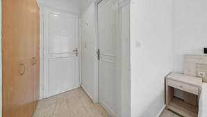 En gang med to hvide døre, en trædør og et lille natbord med en skuffe.