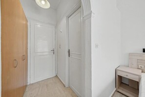 A hallway with two white doors, a wooden door, and a small bedside table with a drawer. - Bed and Breakfast 'The Kavos Sandy Inn-Double Room' with Shared Pool, Wi-Fi and Air Conditioning (Kavos)