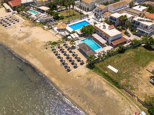 An aerial view of a coastal hotel with multiple swimming pools, sun loungers, and a beach area. - Bed and Breakfast 'The Kavos Sandy Inn-Double Room' with Shared Pool, Wi-Fi and Air Conditioning (Kavos)