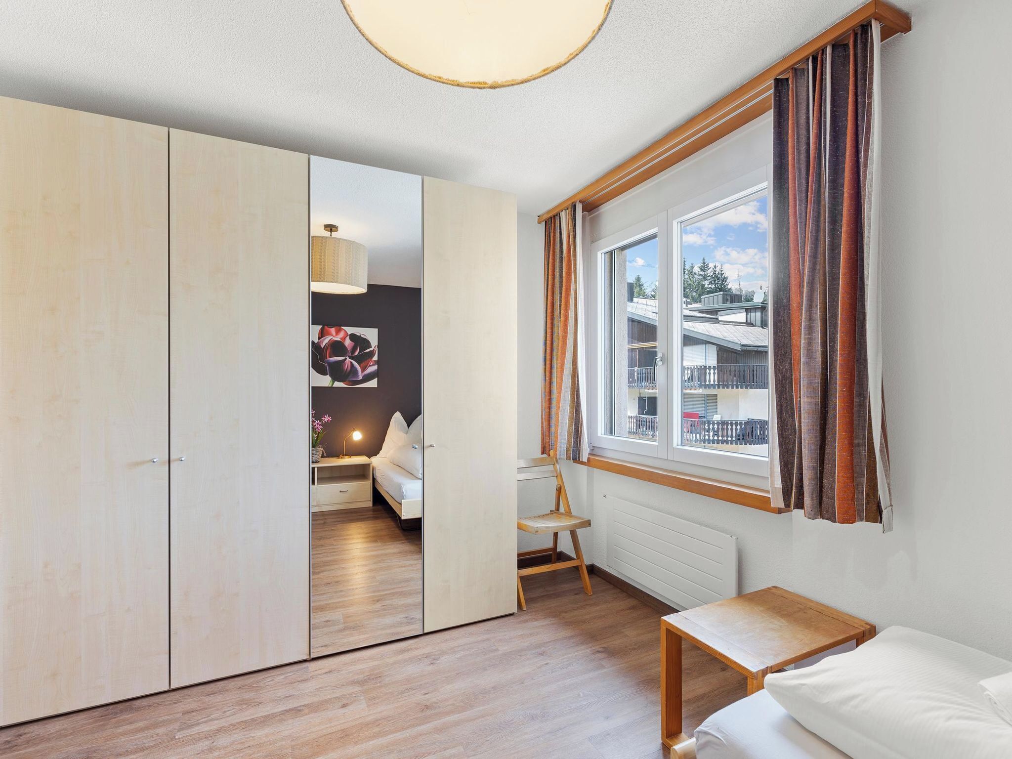 Une pièce comprenant un lit, un bureau, une chaise, une armoire et une fenêtre avec des rideaux.