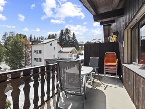 Un balcon avec une table et des chaises, donnant sur un paysage enneigé parsemé de bâtiments et d’arbres.