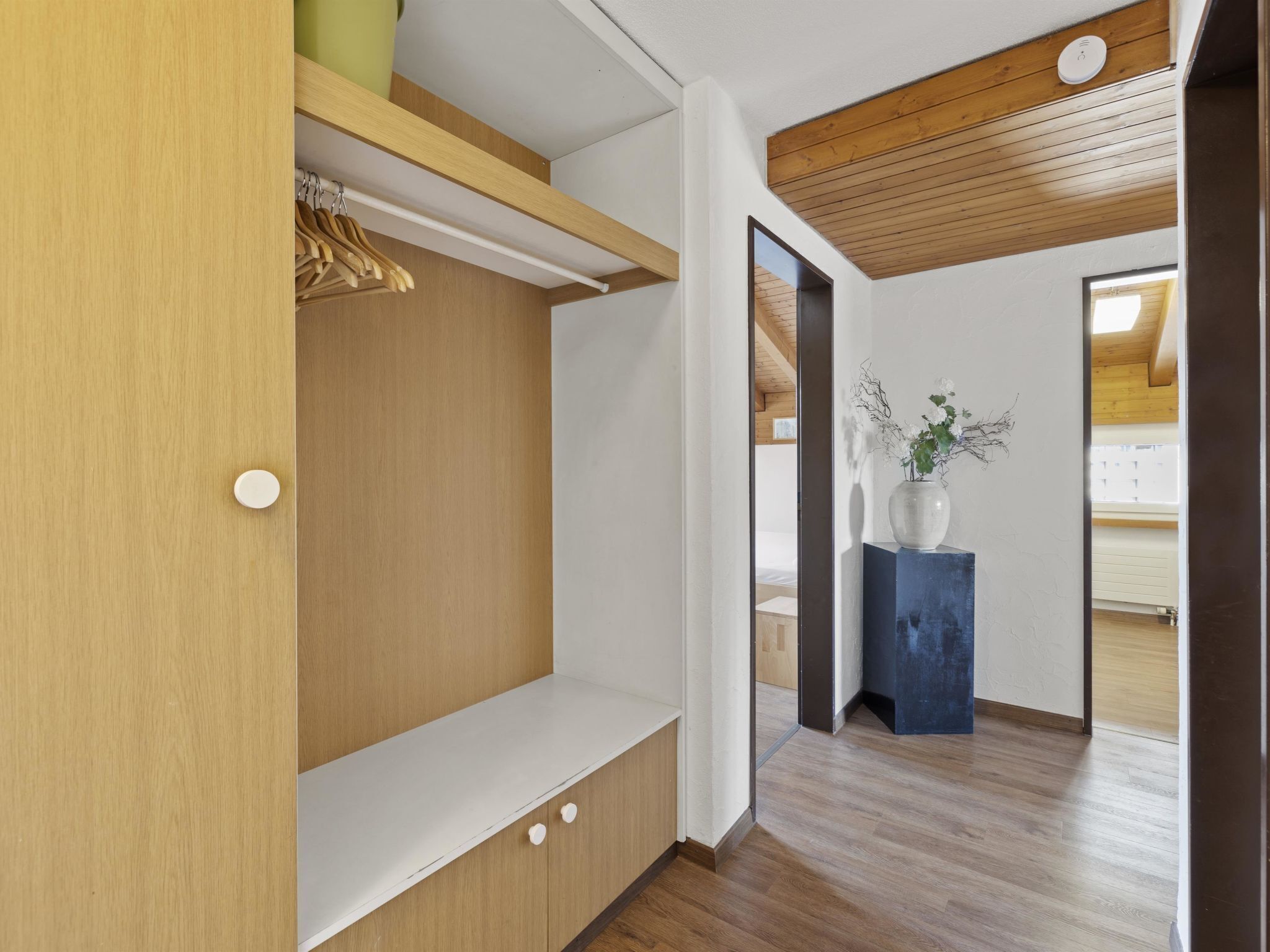 A modern interior with a wooden bench, a hanging rack, and a vase with flowers.