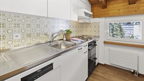 A modern kitchen with white cabinets, a stainless steel sink, a built-in oven, and a window with a view of buildings outside. - A301 Appartement/Fewo,   Ferienwohnung A301 IH by Interhome (Lenzerheide)