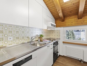A modern kitchen with white cabinets, a stainless steel sink, a built-in oven, and a window with a view of buildings outside. - A301 Appartement/Fewo,   Ferienwohnung A301 IH by Interhome (Lenzerheide)