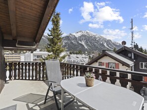 Un balcon avec une table et des chaises, d’où l’on peut admirer une montagne et une ville.