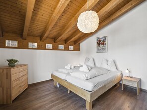 A bedroom with a wooden ceiling, a bed with white bedding, a nightstand, a dresser, and a hanging light fixture. - A301 Appartement/Fewo,   Ferienwohnung A301 IH by Interhome (Lenzerheide)
