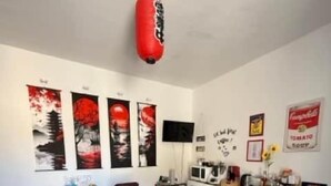 Een eetgedeelte met een houten tafel en stoelen, een bokszak en kunstwerken aan de muur.
