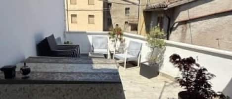 Terraza en la azotea con mesa, sillas y plantas en macetas.