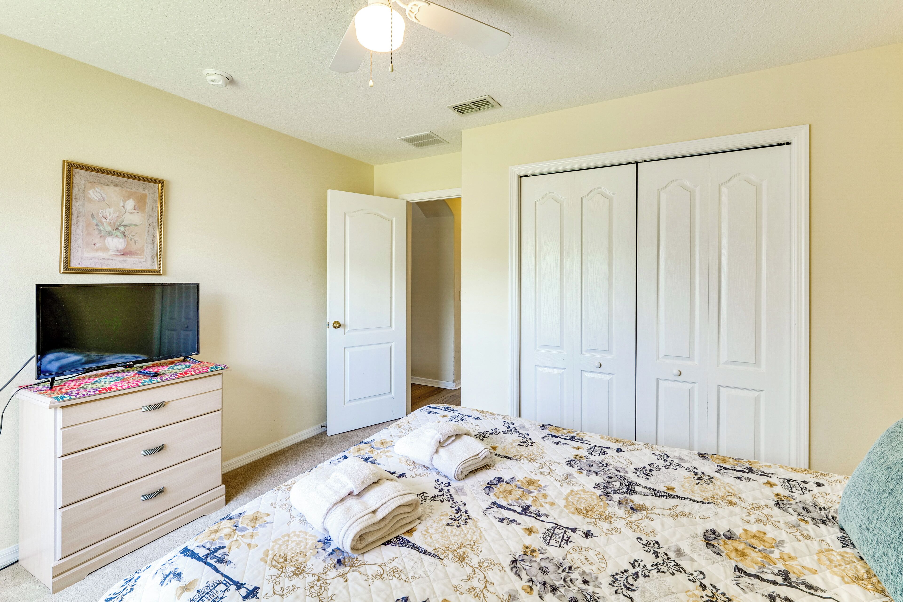 A bedroom with a bed, a dresser, a television, and a door leading to another room.