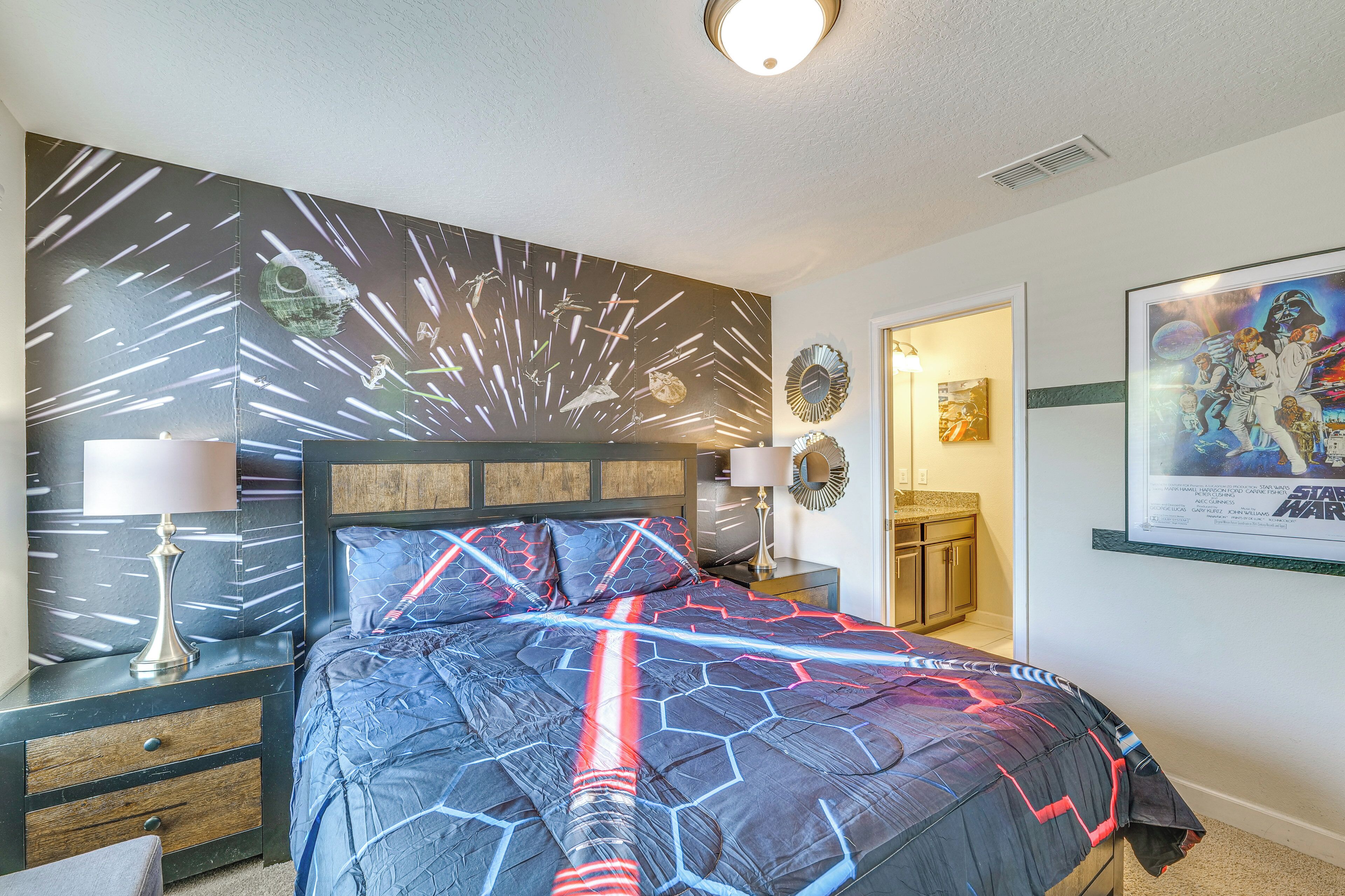 Un dormitorio con una colcha temática de Star Wars, una mesita de noche con lámpara y un cartel en la pared.