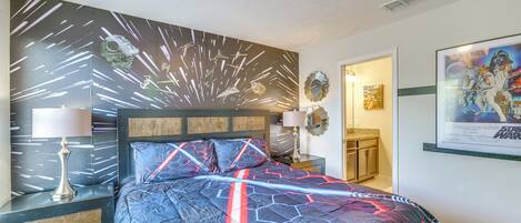 Un dormitorio con una colcha temática de Star Wars, una mesita de noche con lámpara y un cartel en la pared.