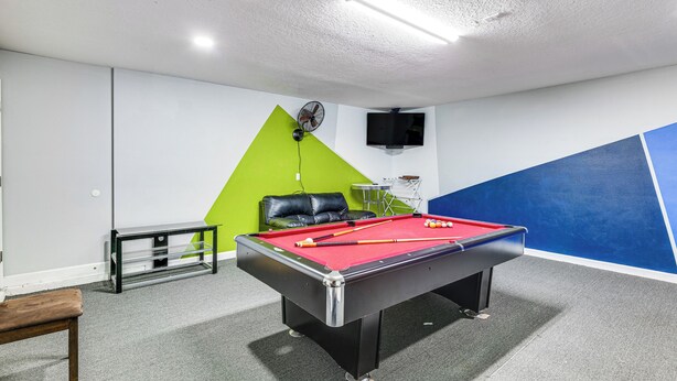 Une table de billard avec des billes, un mur vert, un mur bleu, un plafond blanc et un canapé en cuir noir.