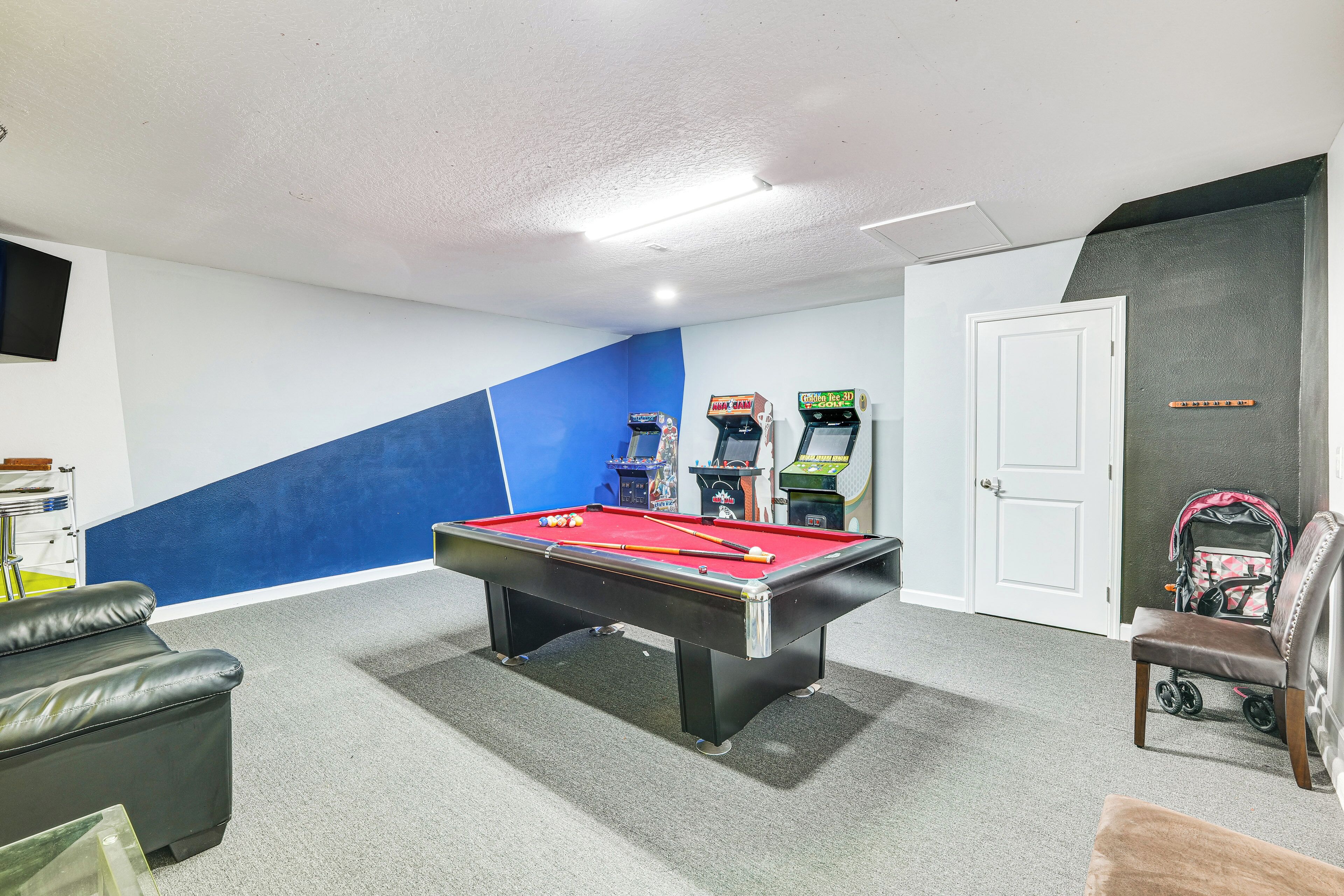 A pool table in a room with a blue wall, a door, and two arcade machines.