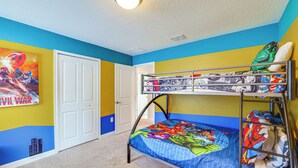 Un lit superposé avec une couette aux motifs de super-héros, une porte et un mur orné d’une fresque murale dans le style d’une bande dessinée.