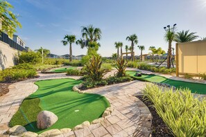 Ein Minigolfplatz mit grünem Kunstrasen, Palmen und Steinwegen.