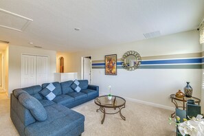 Ein Wohnzimmer mit einem Ecksofa, einem Glastisch, einem Ziertegels und einem Bild an der Wand.