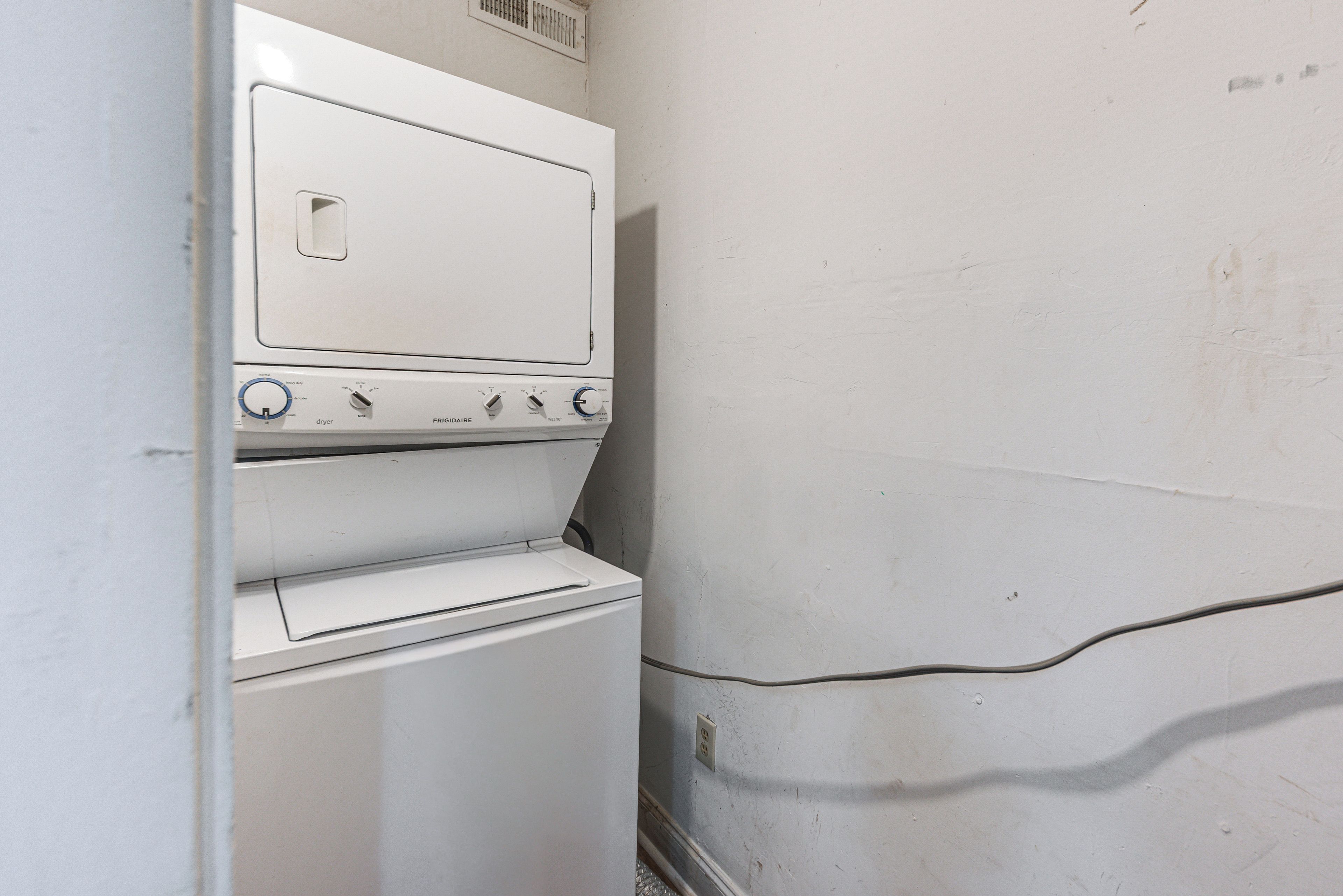 Un electrodoméstico blanco de dos puertas, con perillas de control y un dial, probablemente una lavadora y secadora, en una habitación con una pared lisa y un enchufe visible.