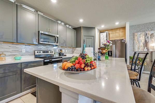 A modern kitchen with grey cabinets, a stainless steel microwave, and a fruit bowl on the island. - At Home Away From Home in Zhills (Zephyrhills)