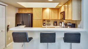 A kitchen with wooden cabinets, a refrigerator, a coffee maker, and three bar stools. - Pool Access & Balcony! Colorado Springs Getaway (Colorado Springs)
