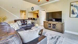 A living room with a leather sofa, a wooden entertainment center, a ceiling fan, and a large flat-screen TV. - Pool Access & Balcony! Colorado Springs Getaway (Colorado Springs)