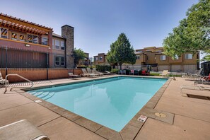 A swimming pool with lounge chairs and a stone building with a chimney. - Pool Access & Balcony! Colorado Springs Getaway (Colorado Springs)