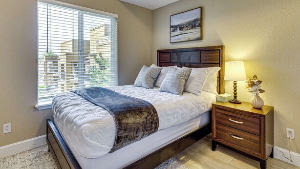 A bedroom with a bed, bedside table, lamp, and a painting on the wall. - Pool Access & Balcony! Colorado Springs Getaway (Colorado Springs)