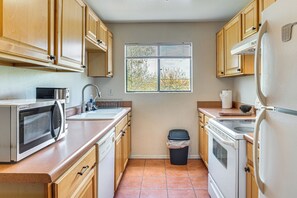 A kitchen with wooden cabinets, a microwave, a sink, a stove, and a trash can.