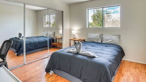 Ein Schlafzimmer mit zwei Betten, einem Spiegel, einem Fenster und einem Schreibtisch mit Stuhl.
