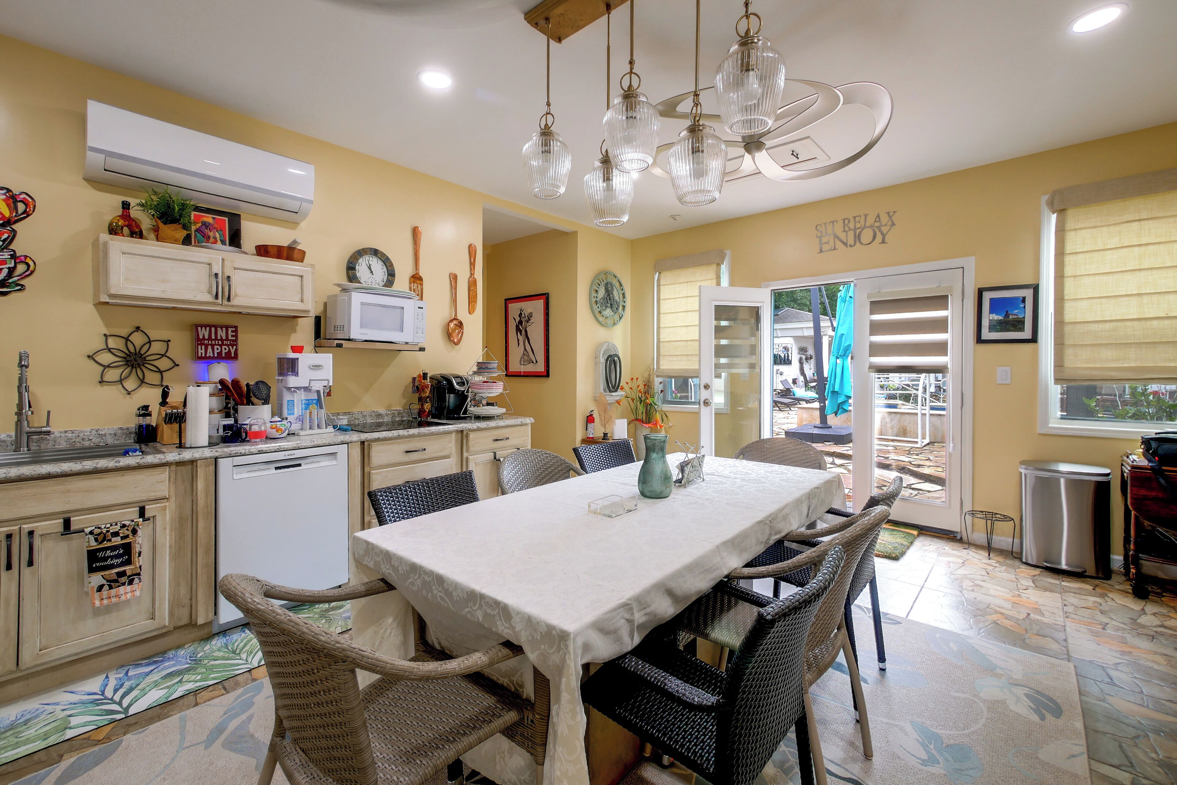 A well-lit kitchen with a dining area, featuring a white table, wicker chairs, and a ceiling fan.