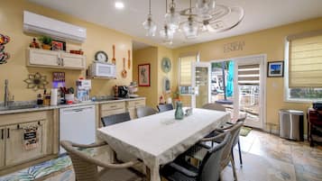 A well-lit kitchen with a dining area, featuring a white table, wicker chairs, and a ceiling fan.